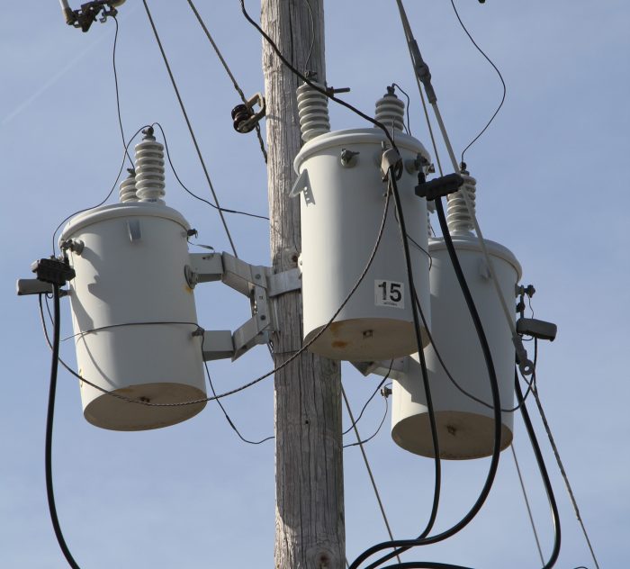 Three White Distribution Transformers on pole with light blue sky